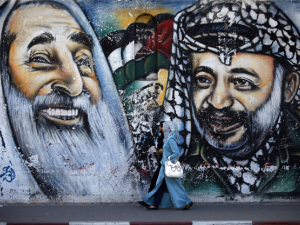 Palestinian women walk past a mural depicting late Hamas spiritual leader Sheikh Ahmed Yassin (L) and late Palestinian leader Yasser Arafat.